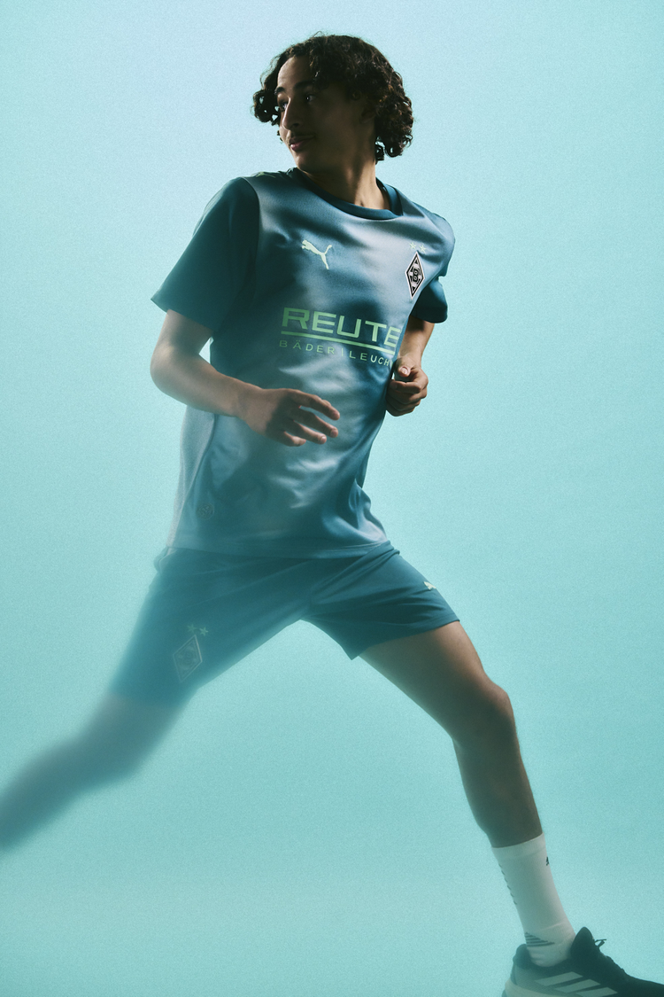 A person running in a blue sports kit with logos, against a turquoise background.