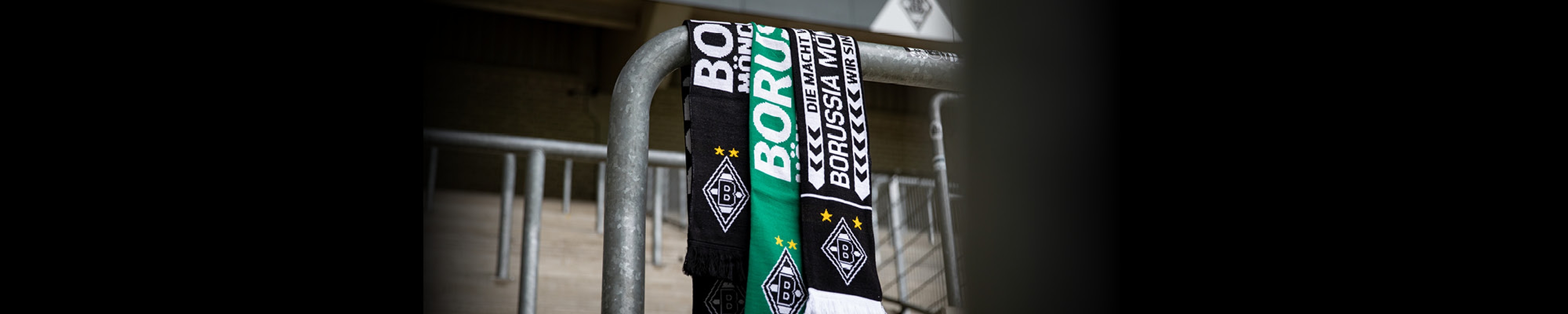 A scarf draped over a metal railing, featuring black and green colors with the text "Borussia" and logo patterns, likely representing a football team.