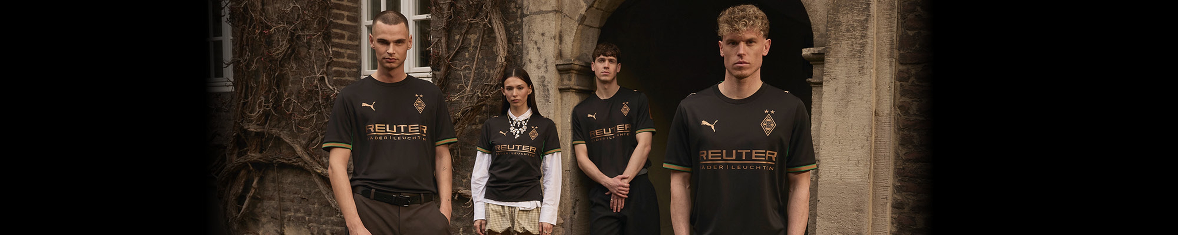 Four individuals in black football jerseys stand in front of an old building with vines, posing for a photo.