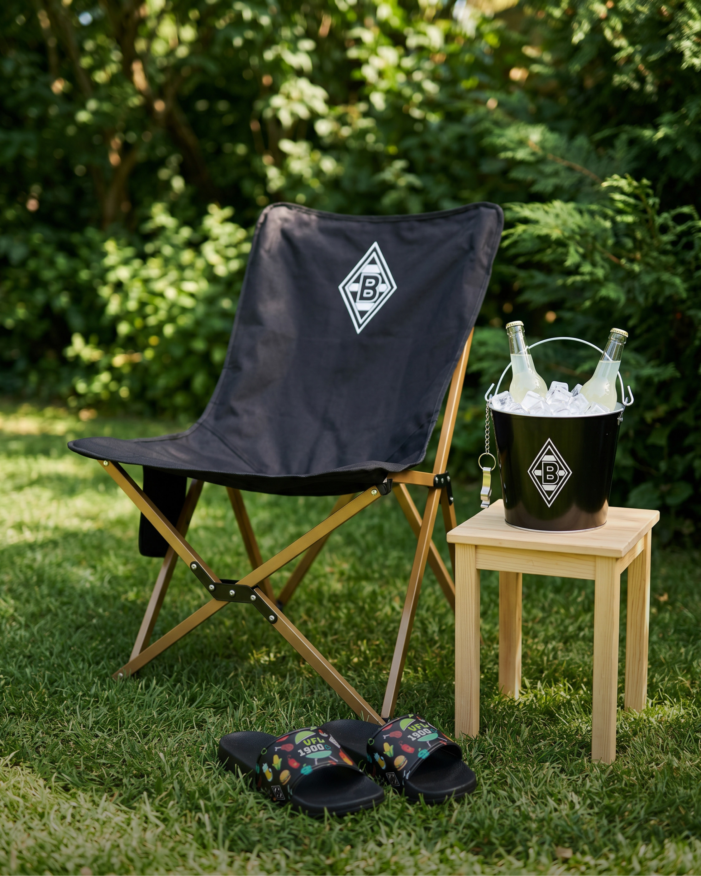 Foldable chair on grass, wooden stool with ice bucket and drinks, and colorful slides, set in a garden background.