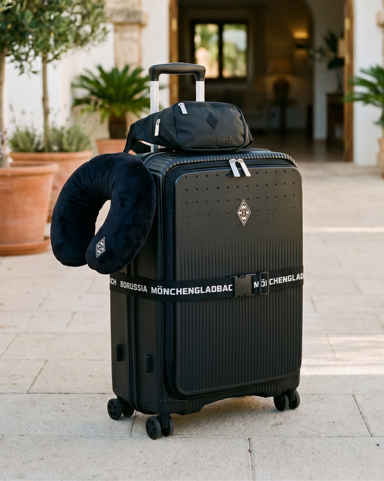 Black suitcase with Borussia Mönchengladbach branding, a neck pillow, and a travel pouch, set on a patio with plants and a building entrance.