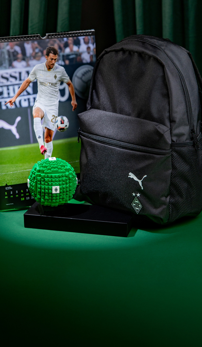 Black backpack and green LEGO soccer ball on a green surface, with a sports calendar featuring a soccer player in the background.
