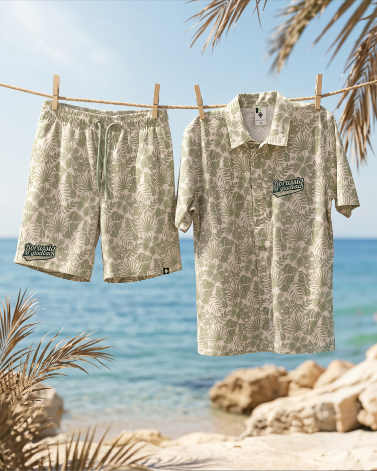 Tropical-patterned shirt and shorts hanging on a clothesline by the beach, with palm leaves framing the scene under a clear blue sky.