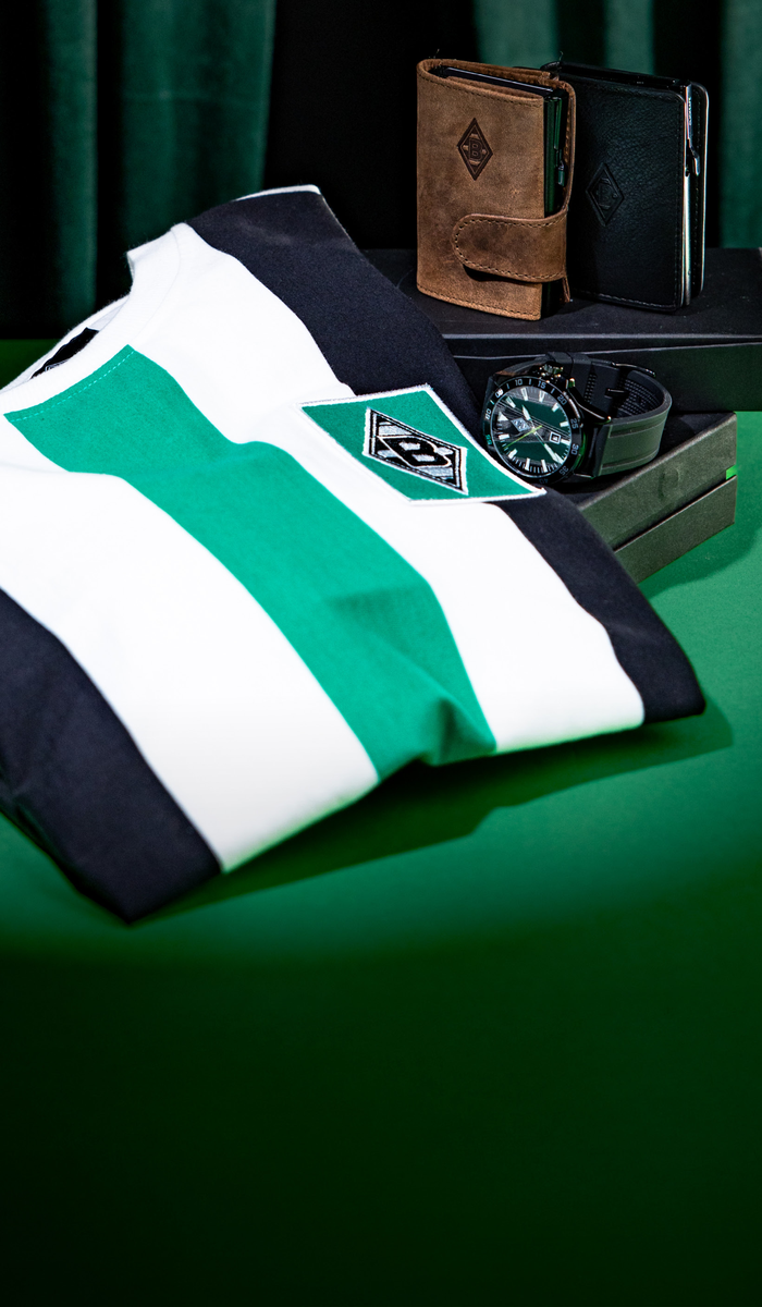 Striped shirt, leather wallets, and a wristwatch displayed on a green surface with a dark green curtain backdrop.