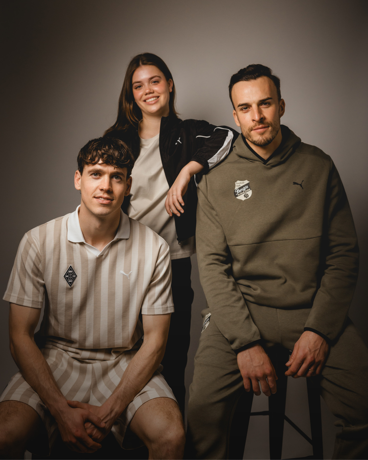 Three people pose in casual Puma outfits against a neutral background; two are seated, one stands behind them, all smiling slightly.