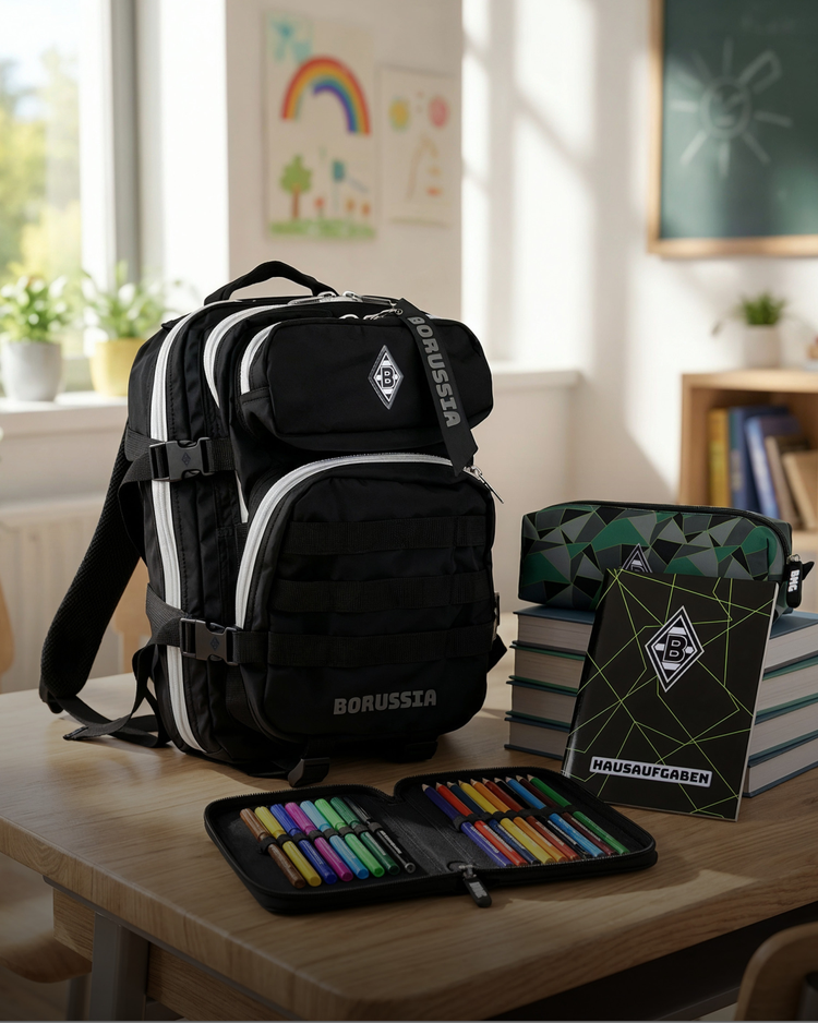 Black backpack on a classroom desk with school supplies including a pencil case, notebooks, and markers. Children's art on the wall behind.