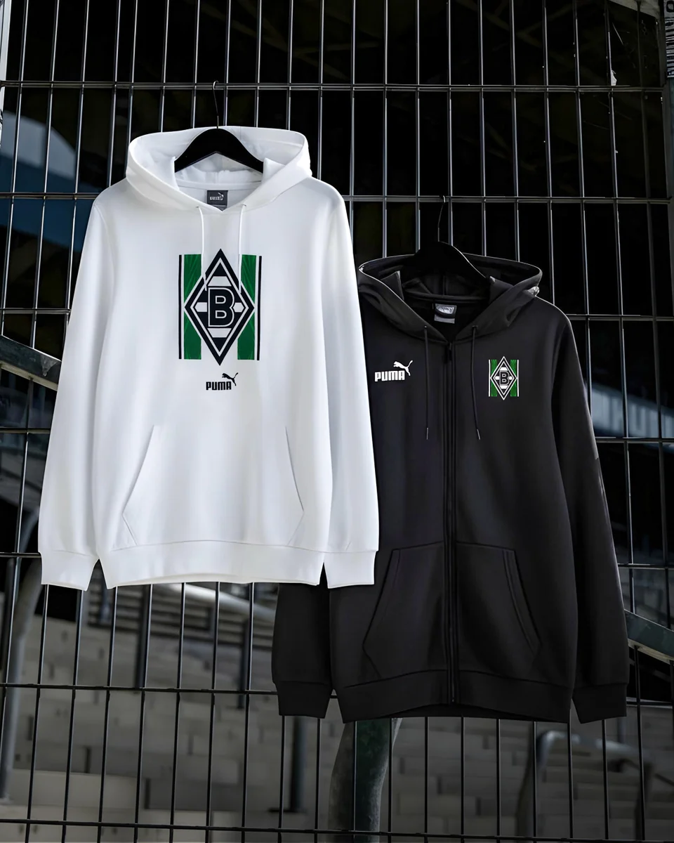 Two Puma hoodies, one white and one black, featuring a green and black geometric logo, hanging against a metal fence background.