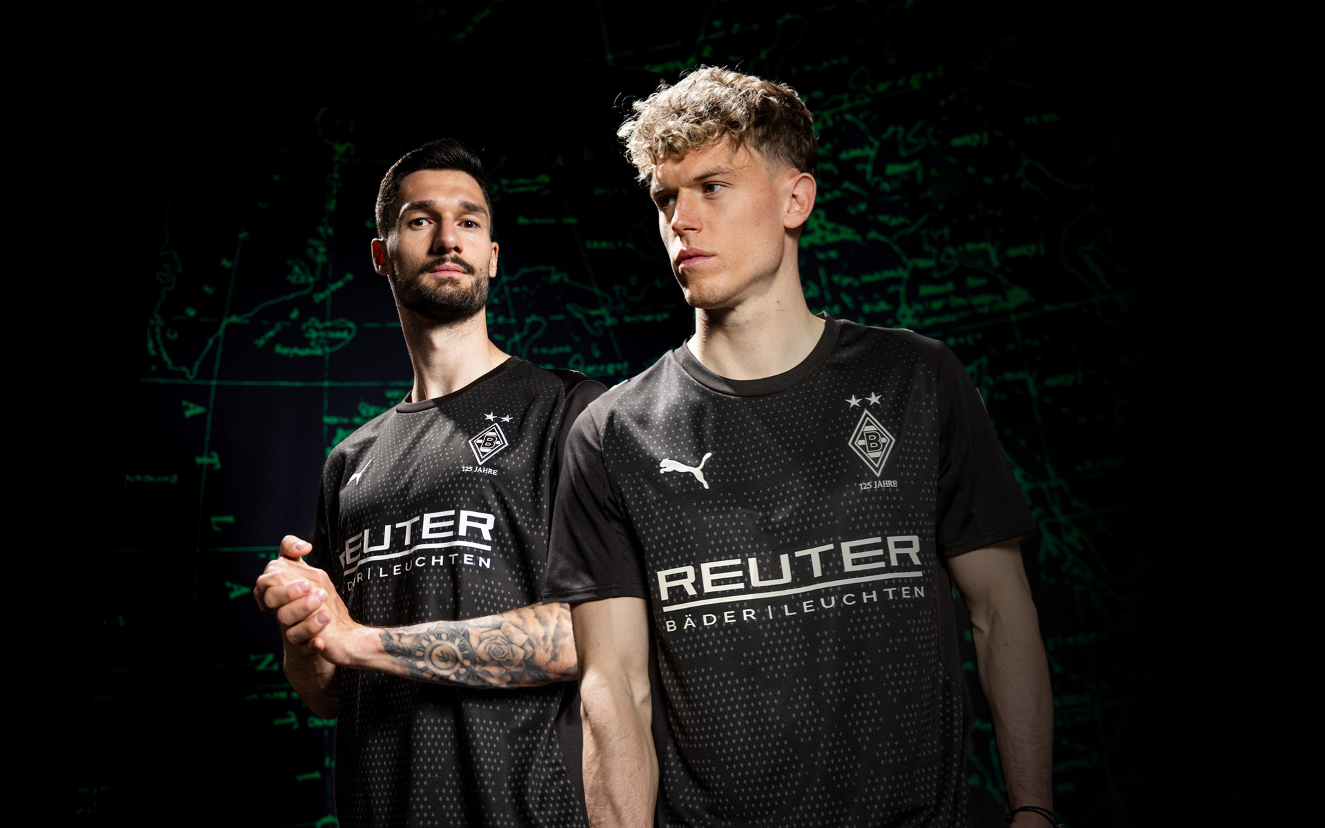 Two soccer players in black jerseys with "REUTER" logo, standing confidently against a dark background with green map lines.