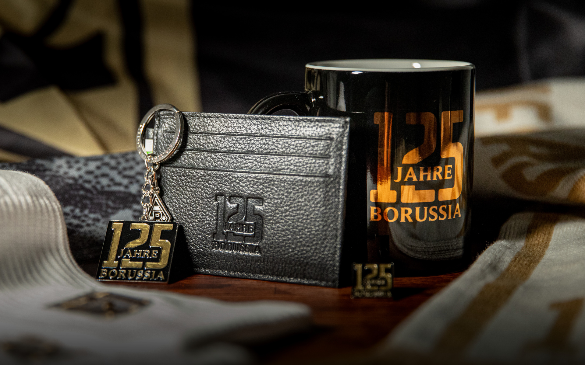 A collection of Borussia-themed items: a black mug, keychain, wallet, and pin, each featuring "125 Jahre Borussia" in gold lettering.
