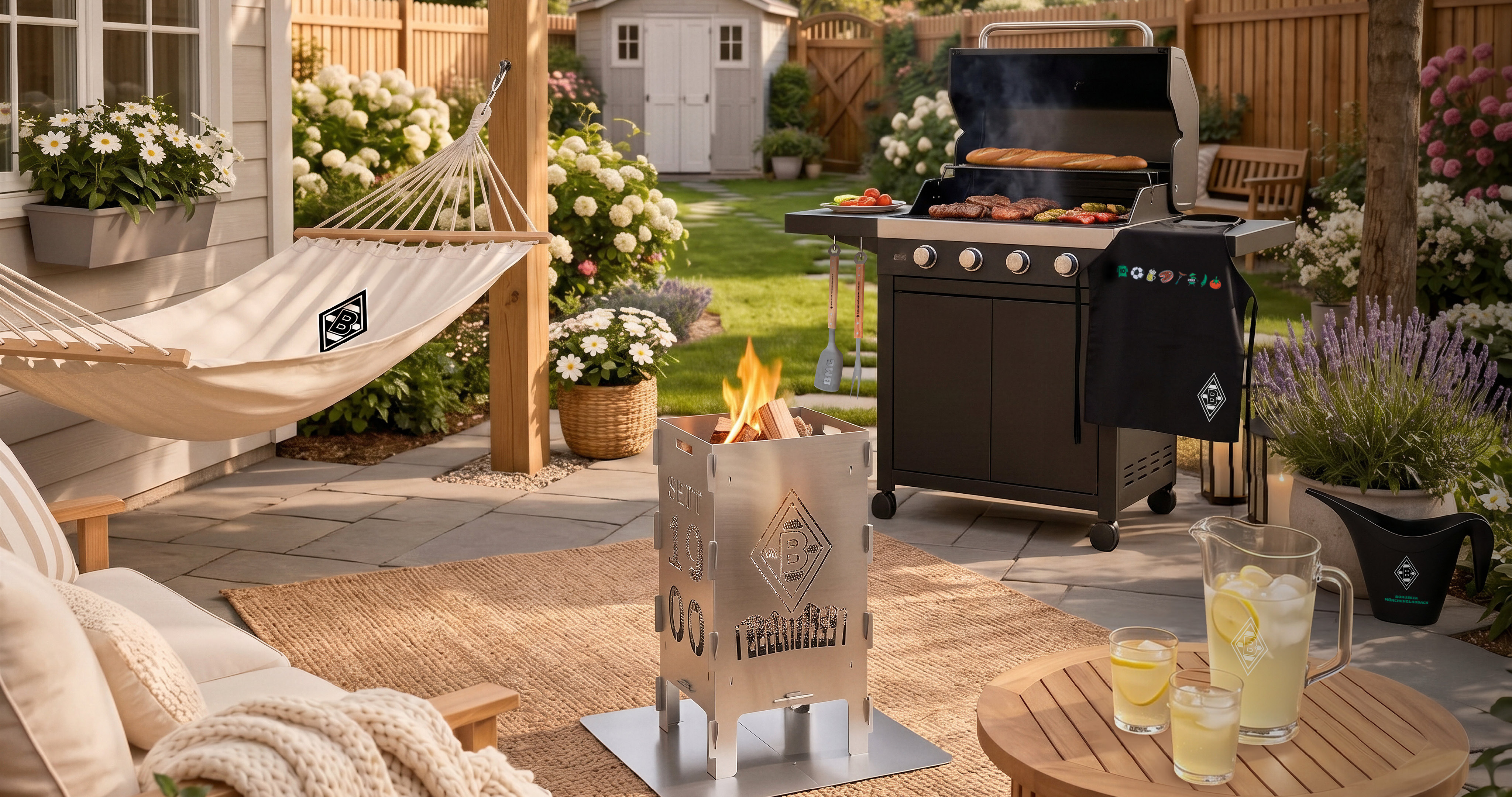Patio scene with a hammock, grill with food, tabletop fireplace, garden, and lemonade on a table. Cushioned seating and blooming flowers decorate the area.