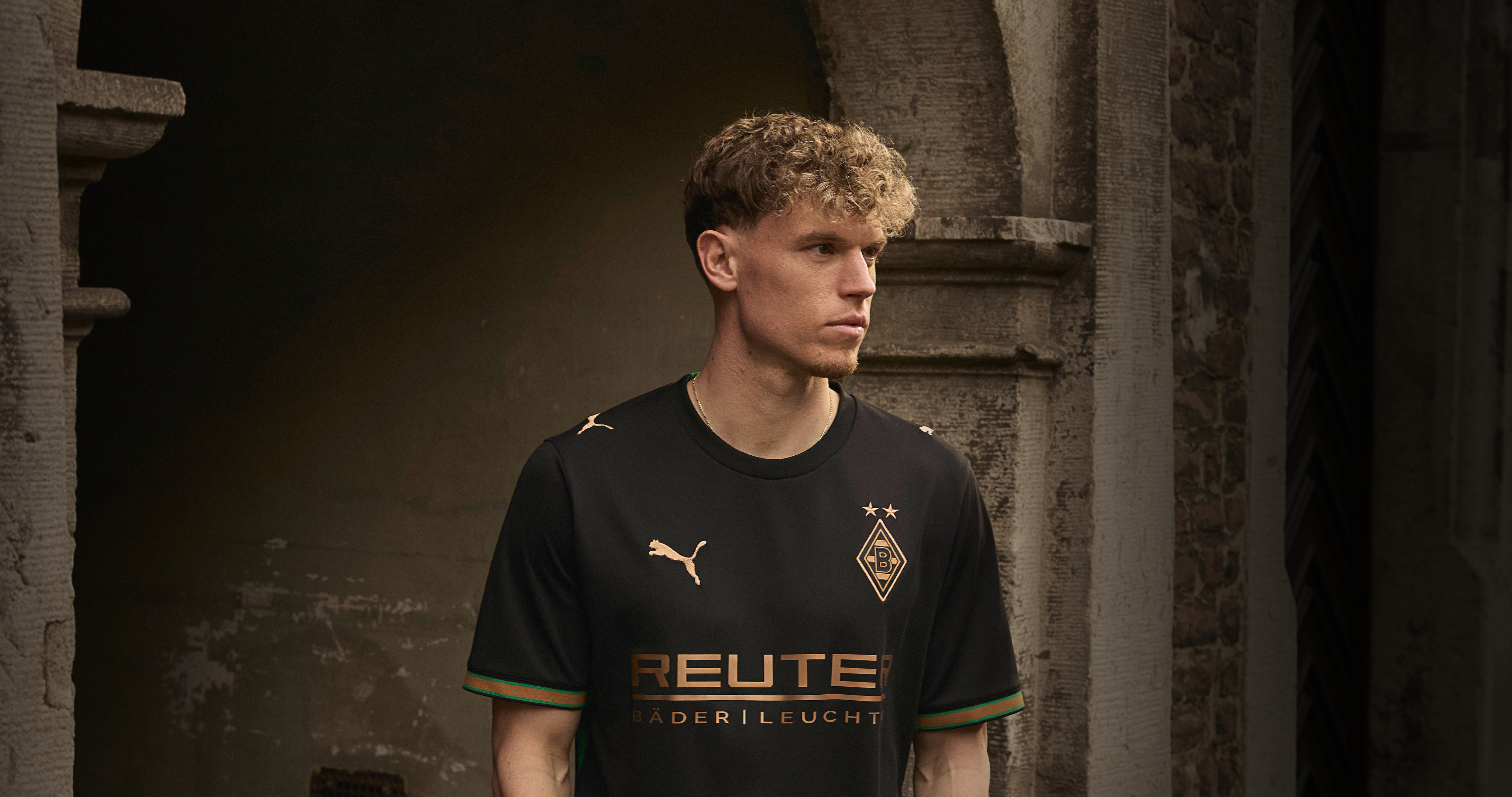 Man in a black Borussia Mönchengladbach jersey with Puma logo, standing in a stone archway.