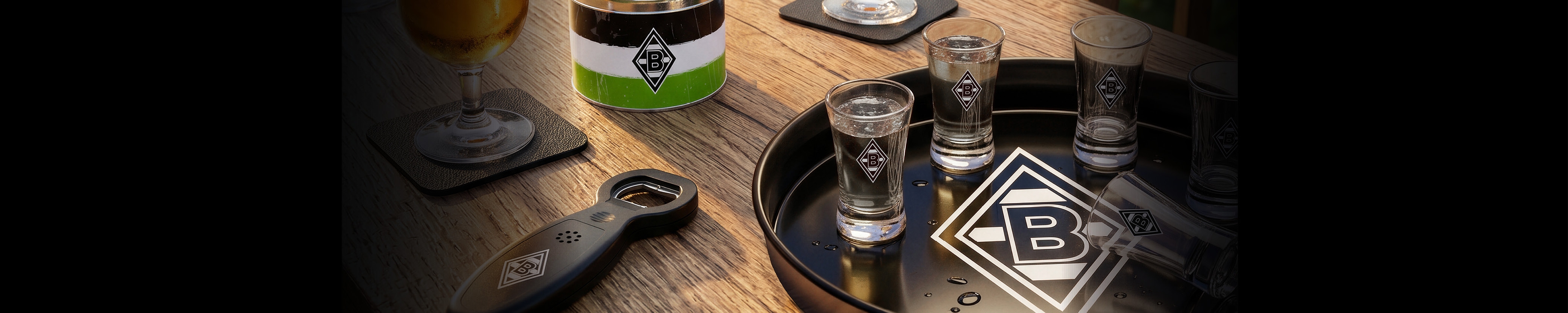 Glasses and a beer on a wooden table, with a tray and bottle opener featuring a logo. A green, white, and black can in the background.