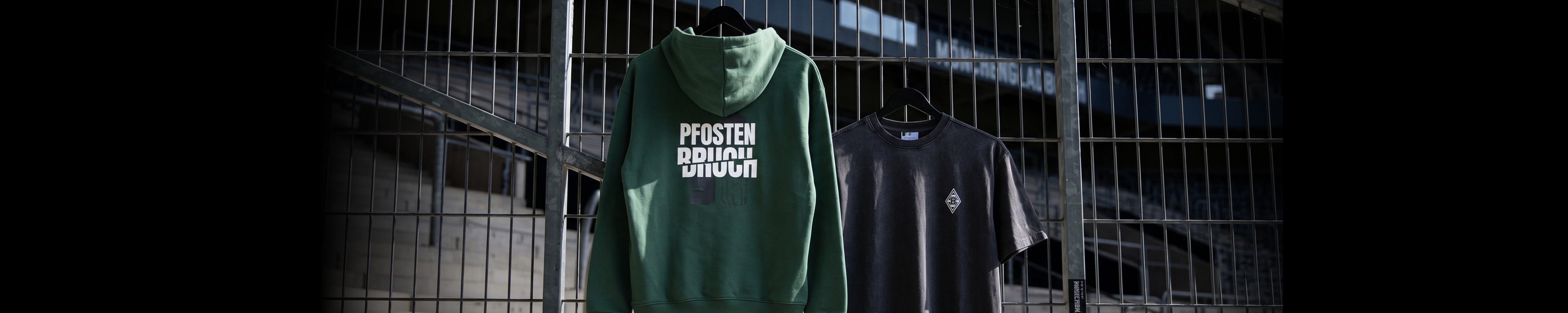 A green hoodie and a black T-shirt hang on a metal fence, with the text "Faster Future Division" visible on the hoodie.