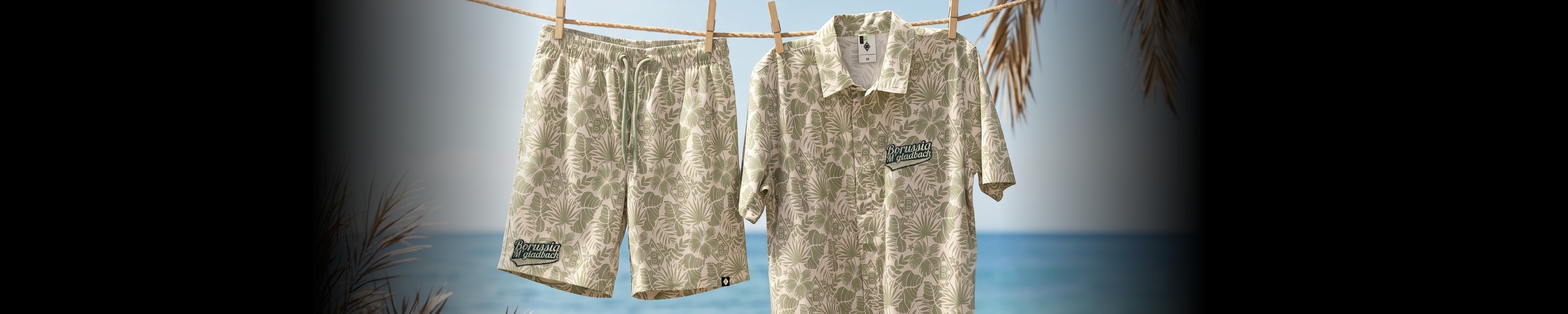 Camo shirt and shorts hanging on a clothesline with a beach and ocean in the background.