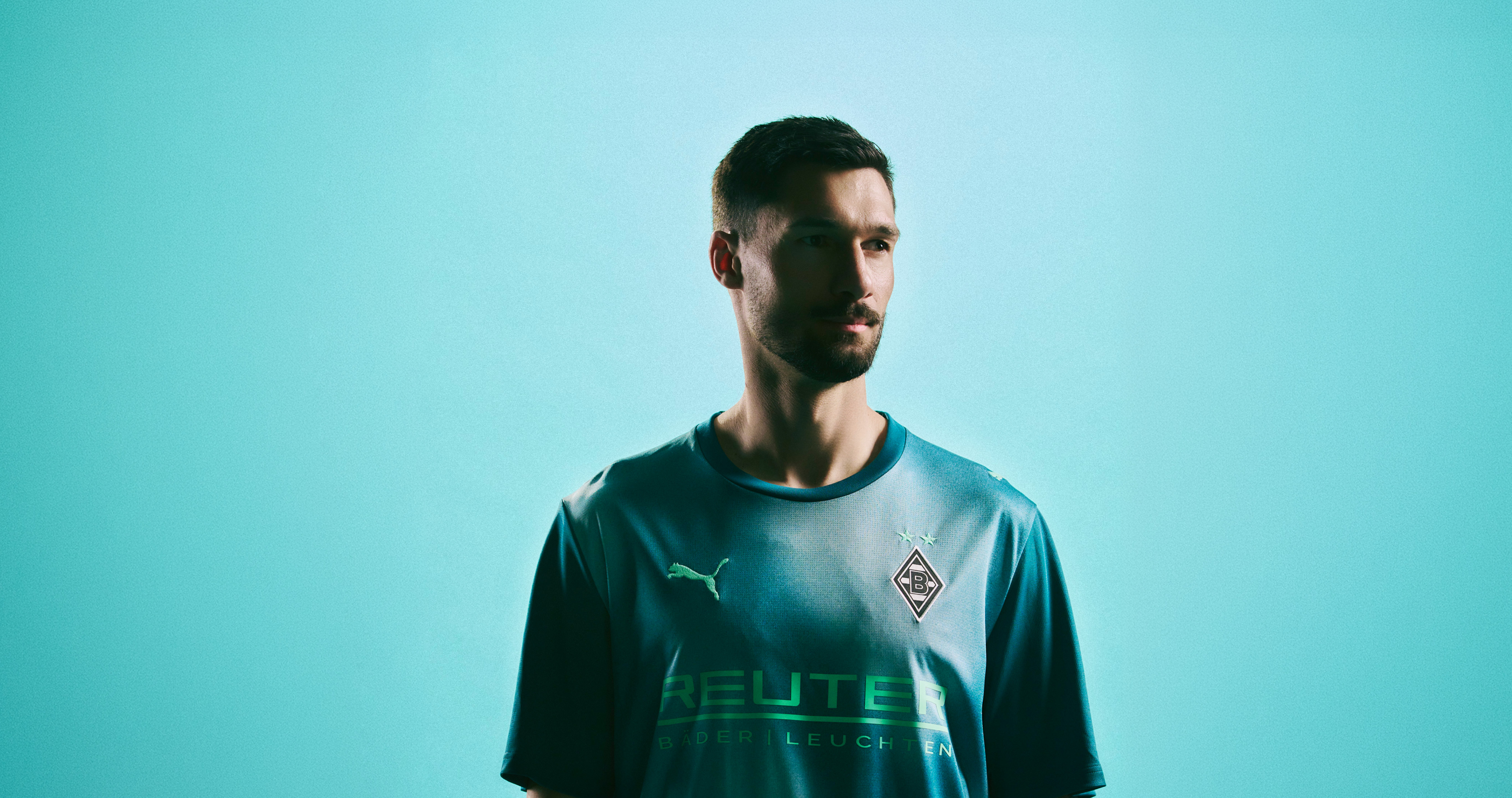 A man in a teal sports jersey stands against a teal background, with a contemplative expression.