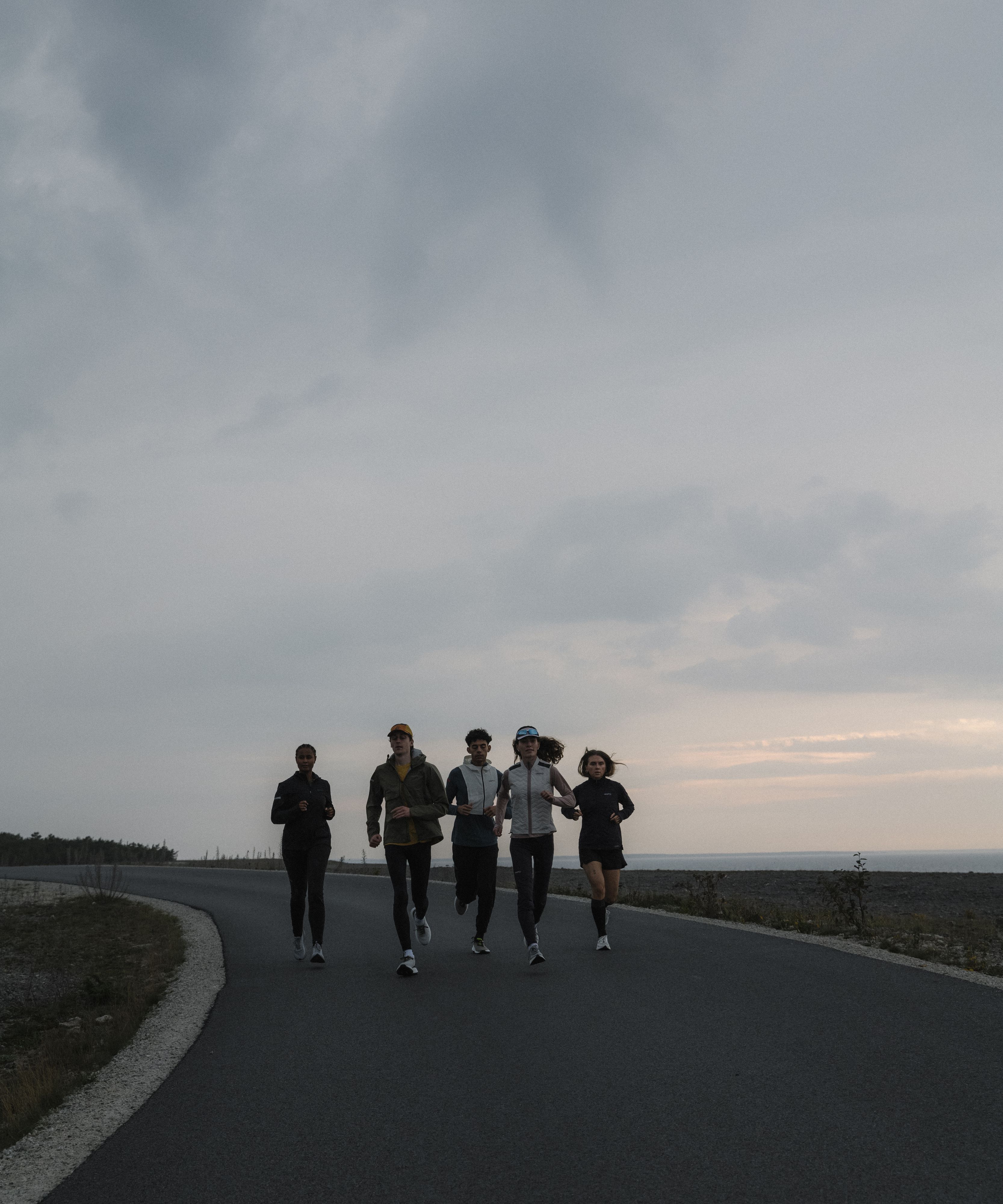 Five people jogging together on a paved road under a cloudy sky, with a horizon in the background.