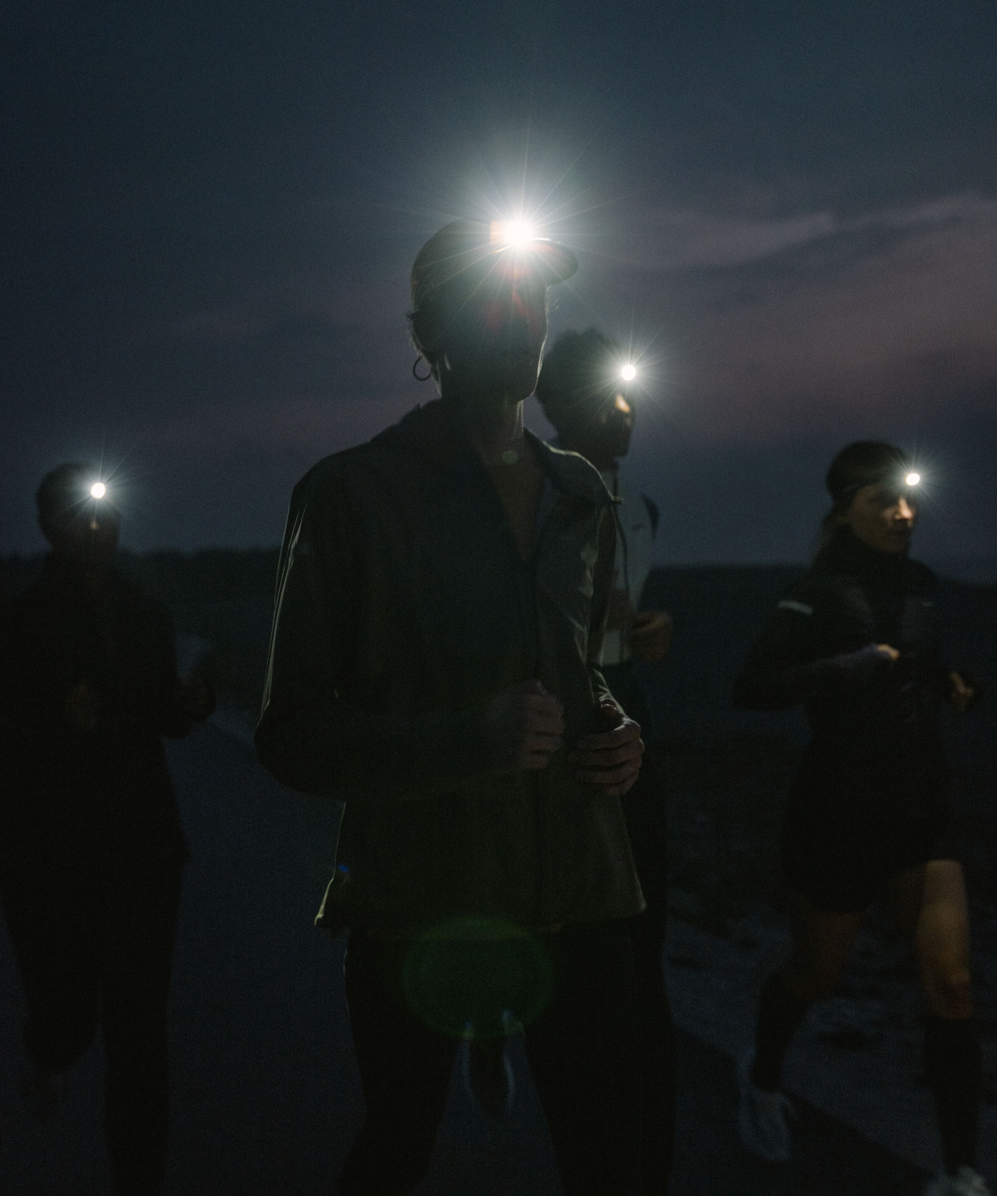 Runners wearing headlamps jog in the dark, their lights illuminating the path ahead under a dusky sky.