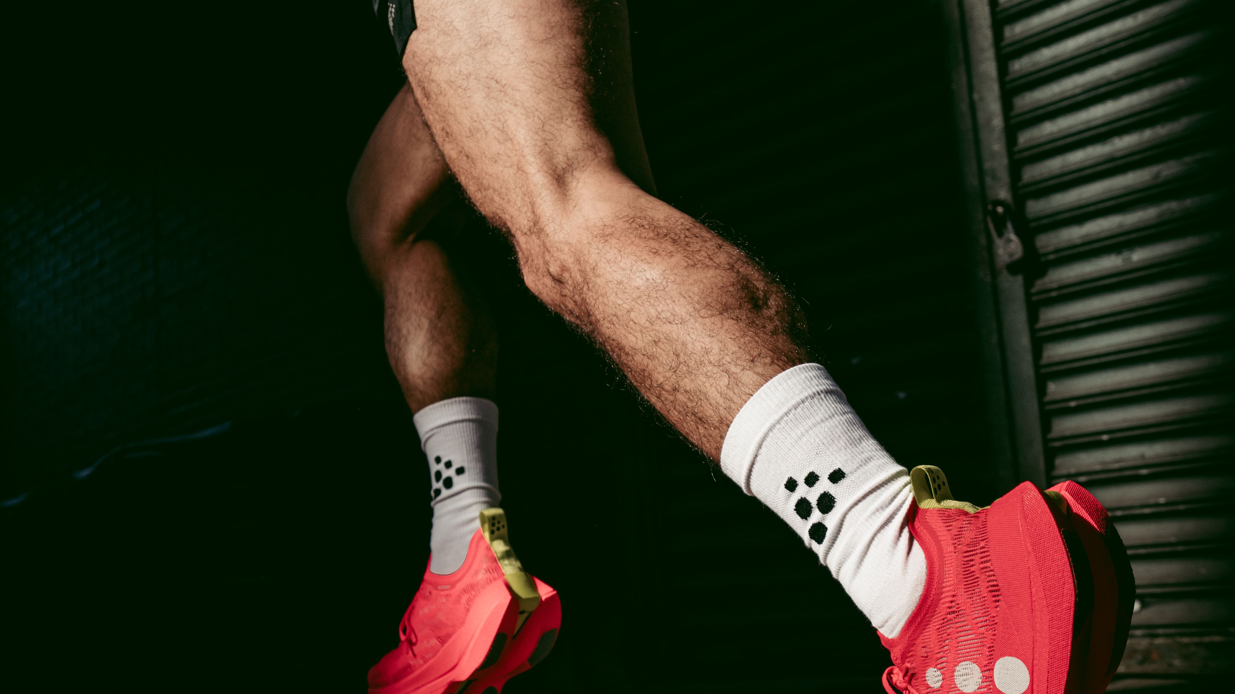 Person running in bright red sneakers and white socks with black dots, wearing black shorts and a light jacket, on a dimly lit street.