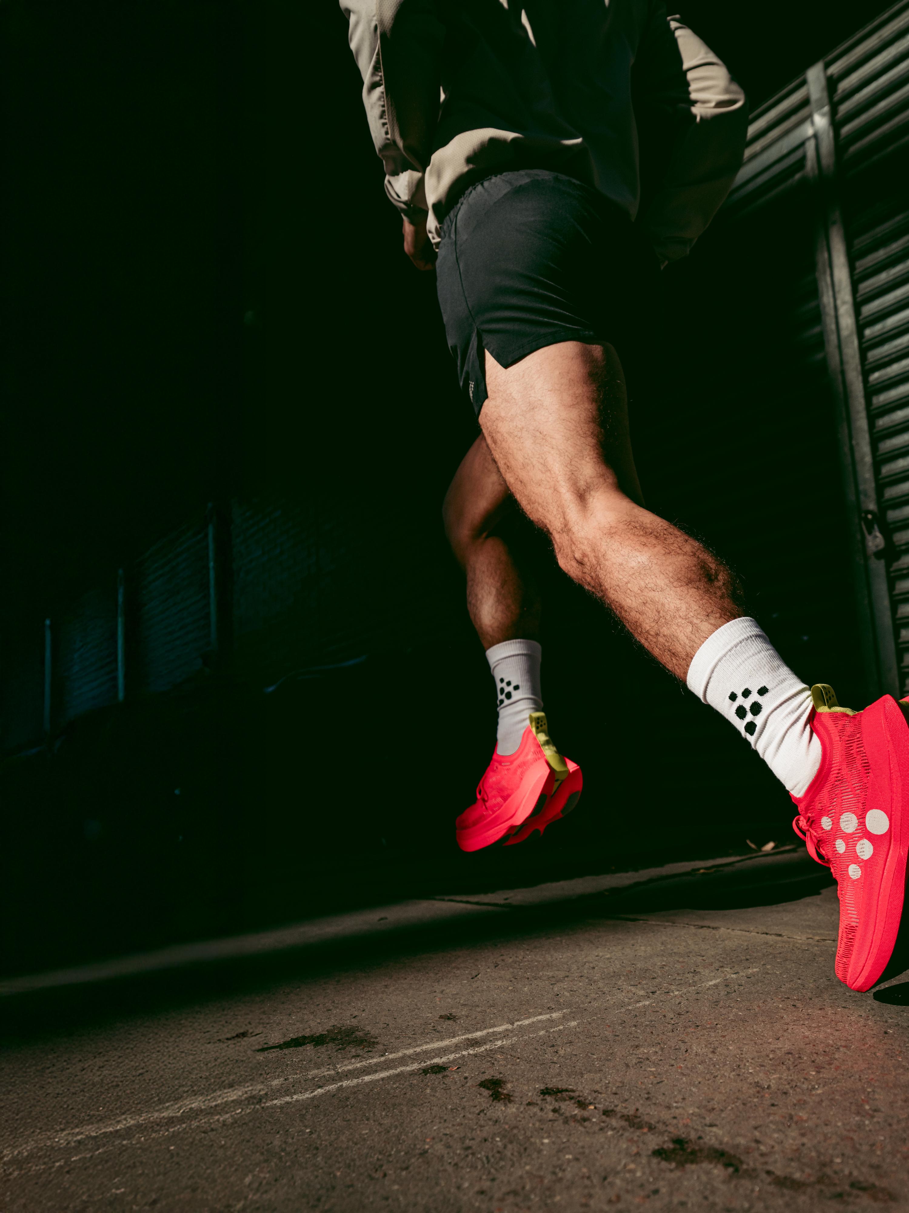 A person running in bright red shoes and white socks with black dots, against a dark urban background.