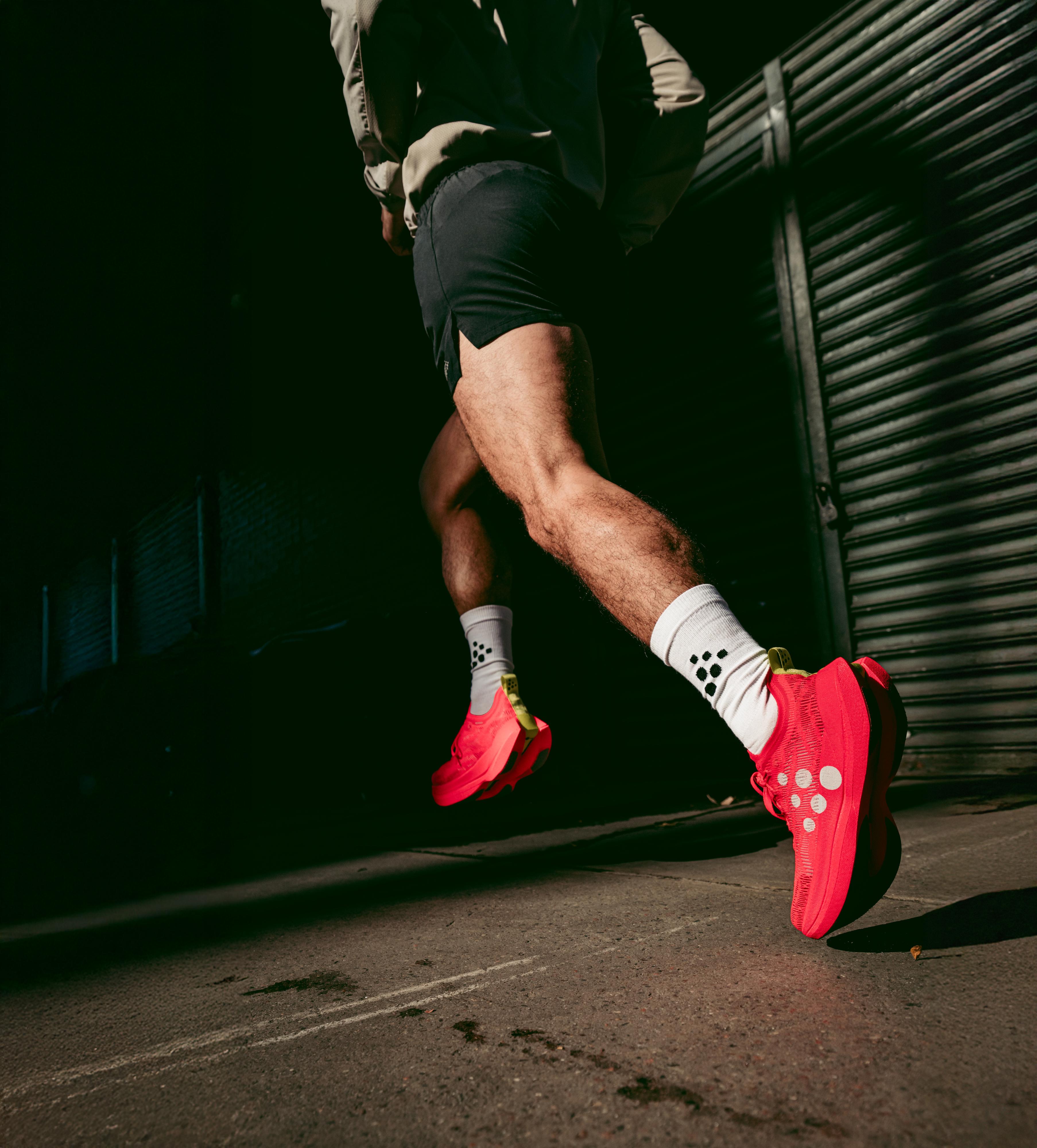 A person running in bright red shoes and white socks with black dots, against a dark urban background.