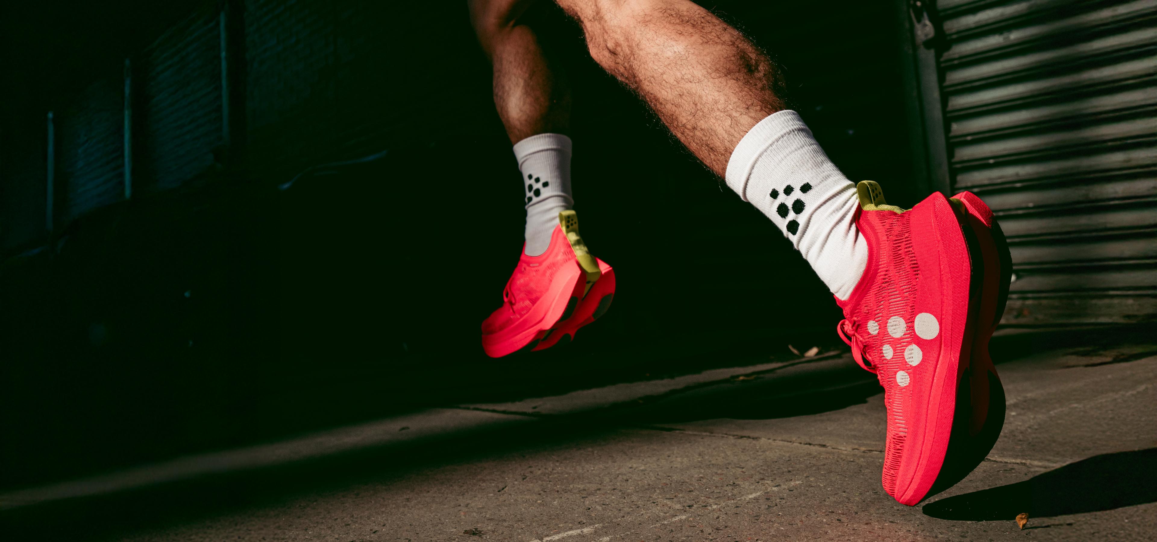 A person running in bright red shoes and white socks with black dots, against a dark urban background.