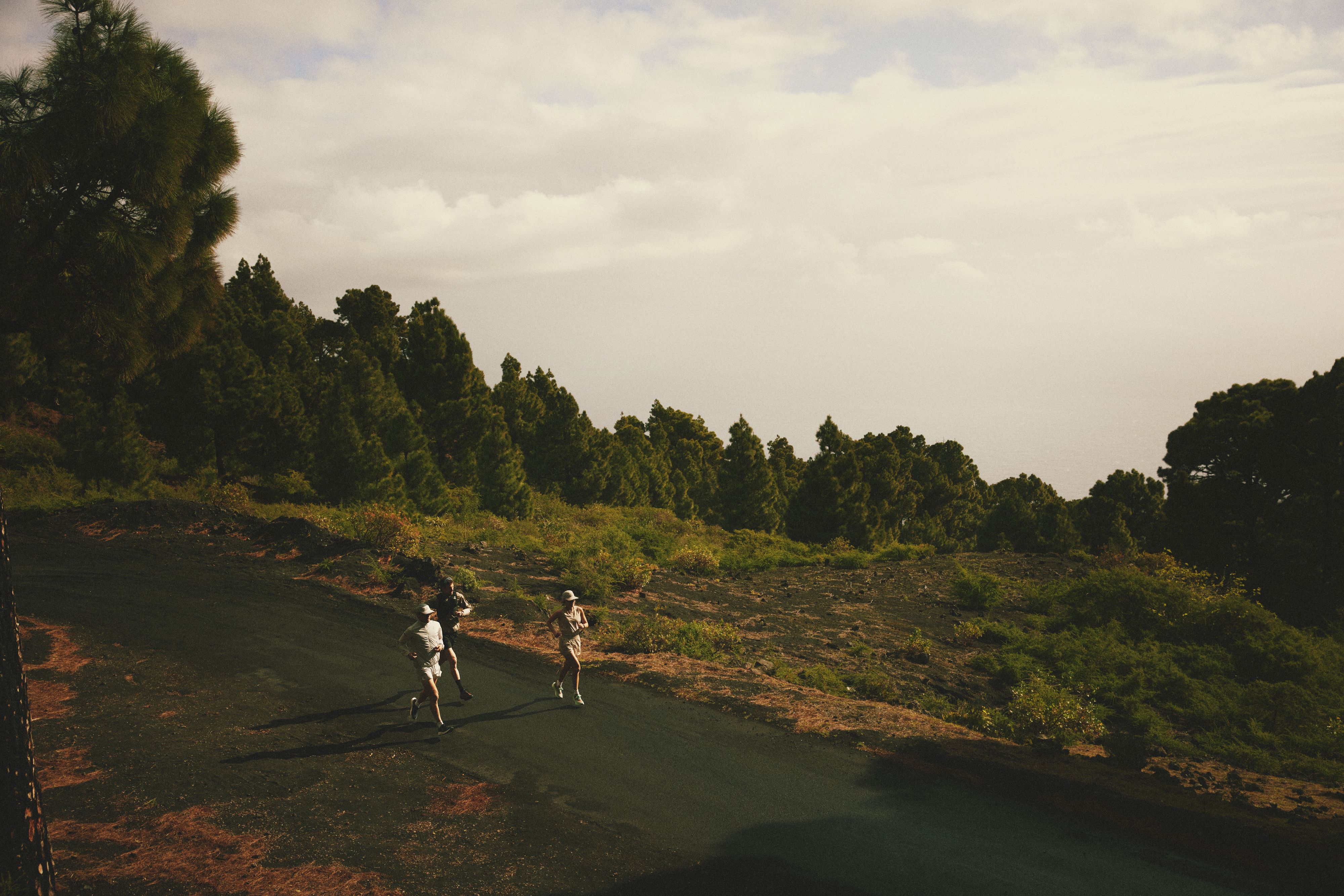 Two people running on a paved path through a lush, hilly landscape with dense trees under a cloudy sky.