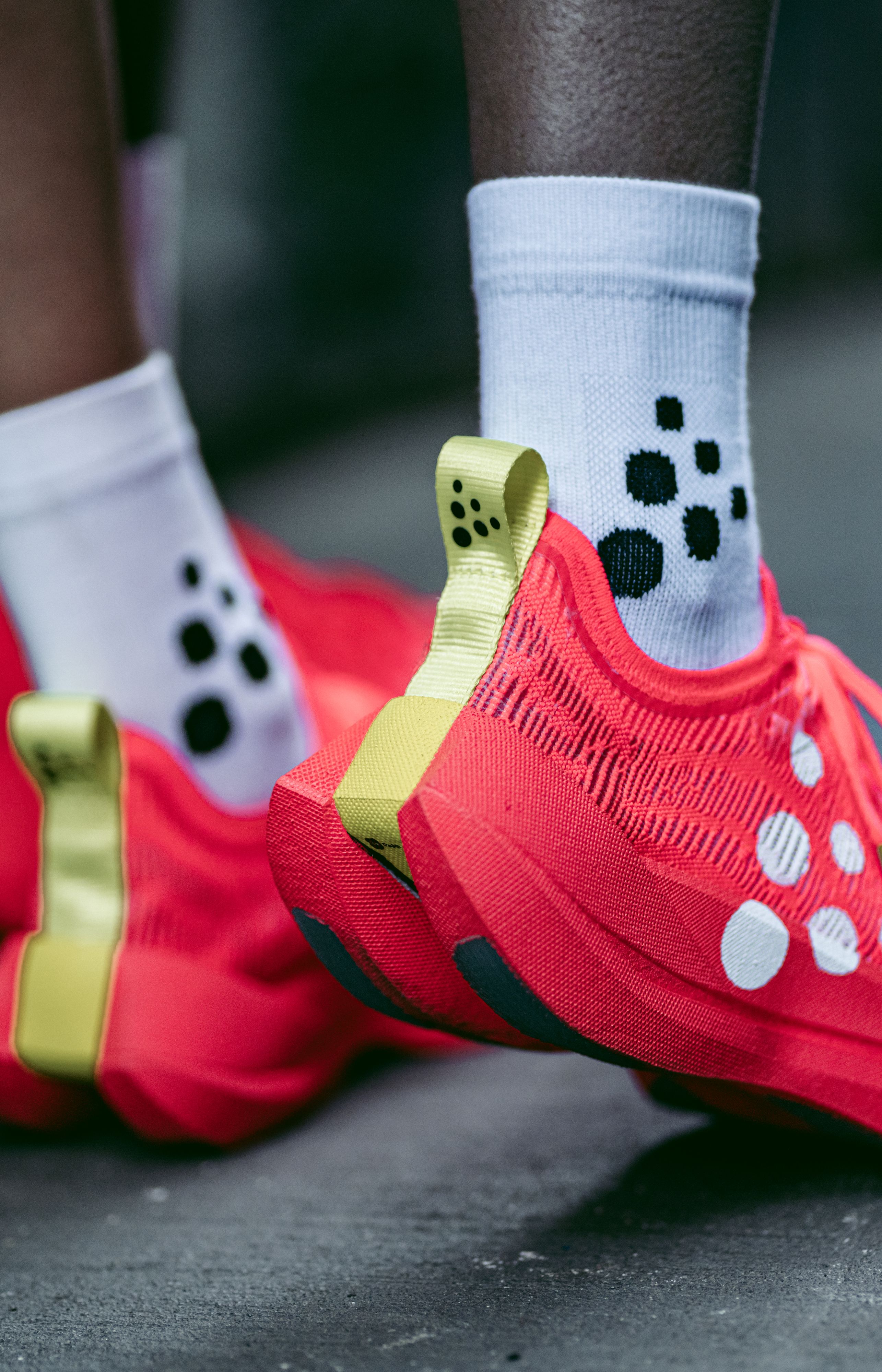 Two people wearing bright red running shoes with yellow accents and white socks featuring black polka dots, walking on a pavement.