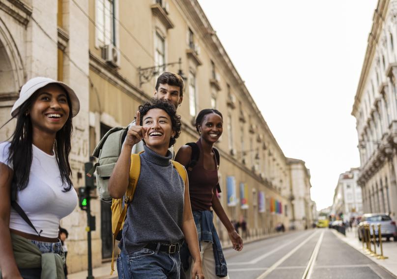 Group of tourists exploring city street and pointing at landmark