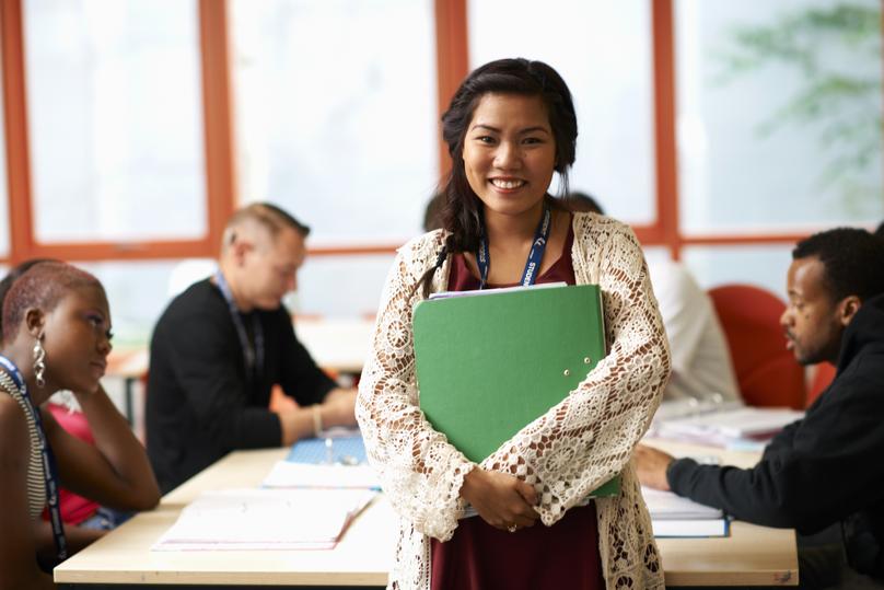Portrait of female student holding file in front of class