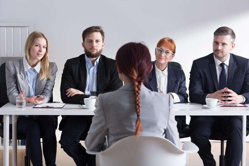 Woman during job interview and four businesspeople sitting by office table
