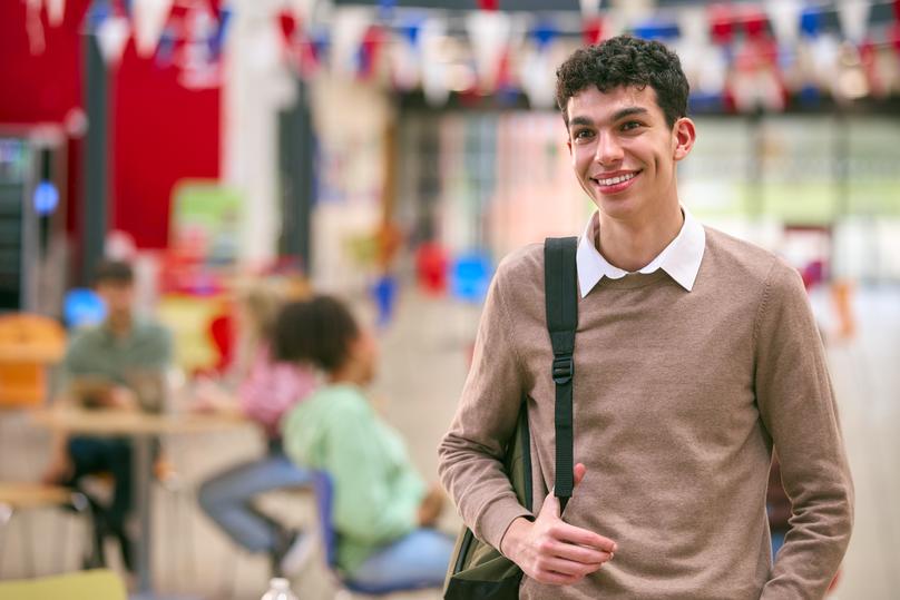 Portrait Of Smiling Male University Student With Bag Standing Inside College Building