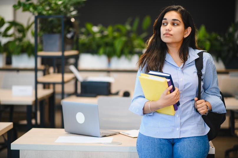 Indian female student standing holding books in campus