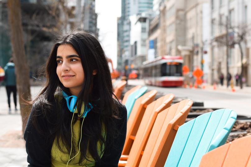 Portrait of young girl sitting on city street with headphones off