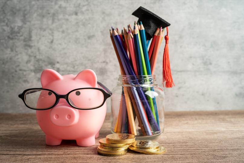 Pigging bank wearing eyeglass with colorful pencils; saving bank education concept.