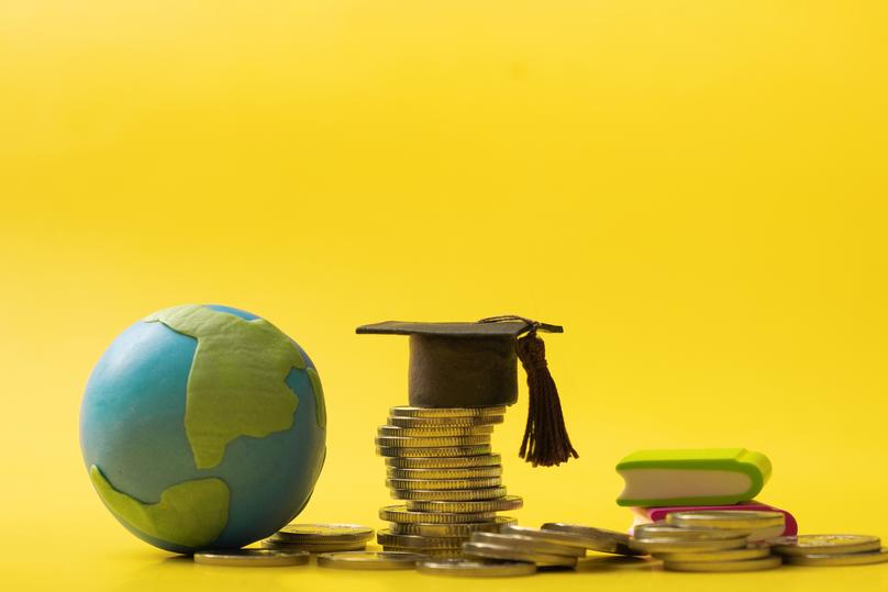 Graduated cap with coins and globe on yellow background. Savings for education concept.