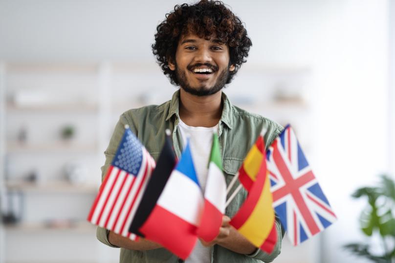 Cheerful indian student holding bunch of flags of various countries and smiling at camera