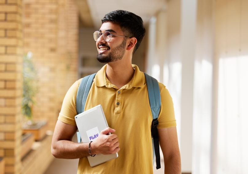 University student, college and indian man with a tablet and backpack while walking down campus cor