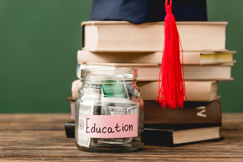 books academic cap and piggy bank on wooden surface isolated on green