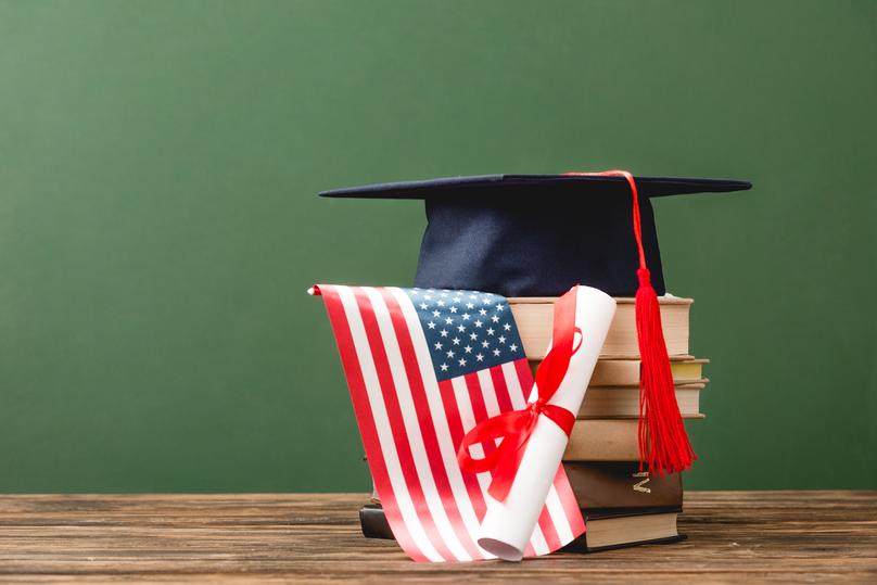 books, academic cap, diploma and american flag on wooden surface isolated on green