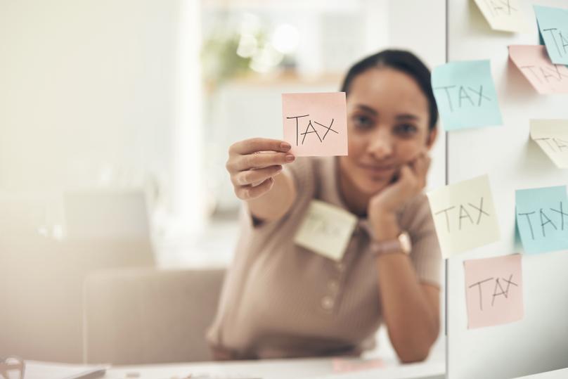 Shot of a young businesswoman holding a note with tax written on it in an office