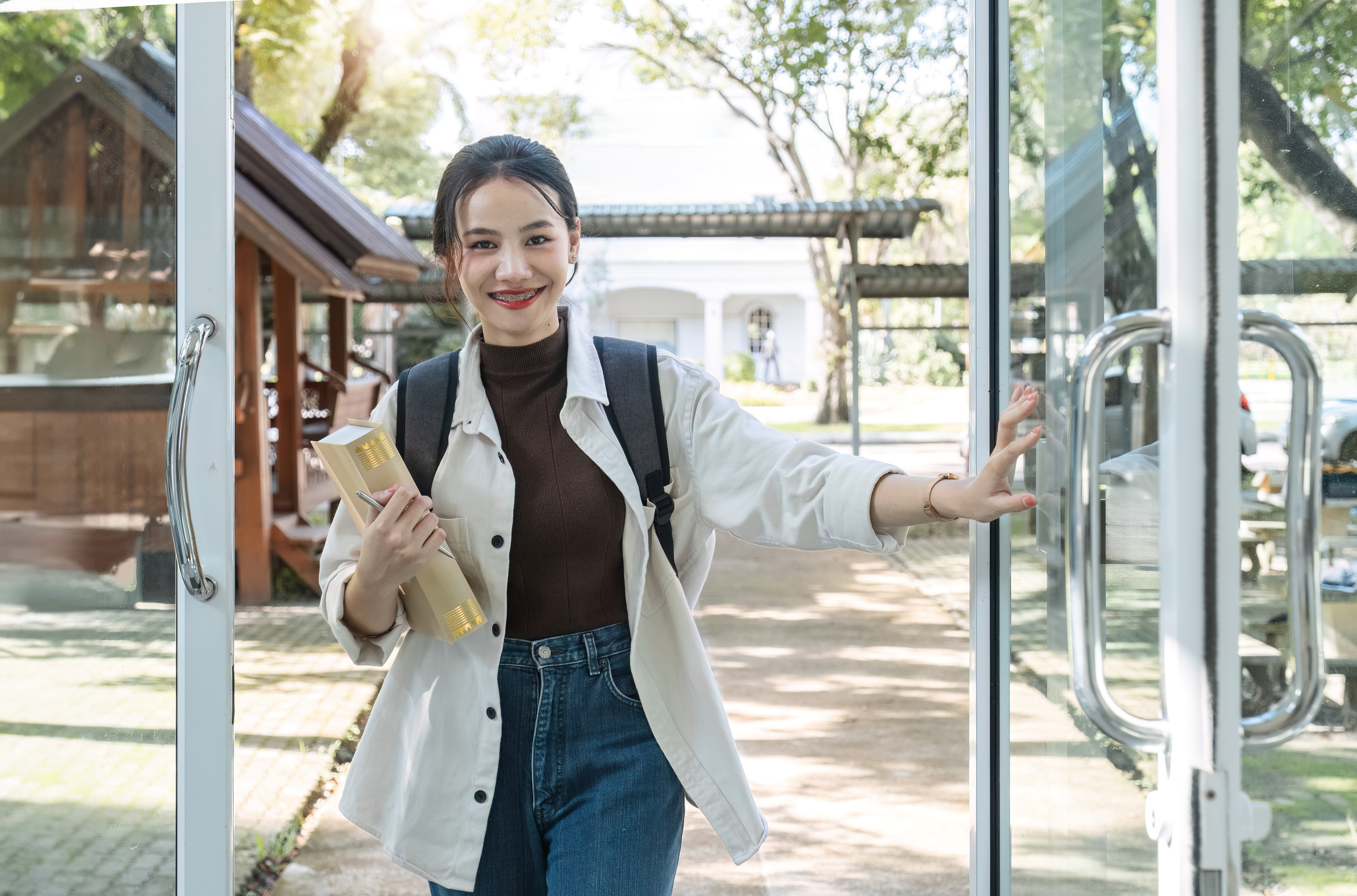 Attractive young Asian female student stands holding a book to make an appointment with a college friend..
