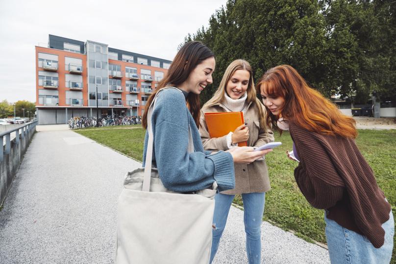 Group of three cheerful female collage students outside their dorm on a cold autumn day, walking on campus to get to their class.