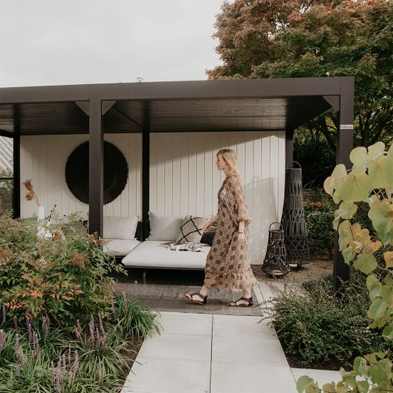 Een vrouw wandelt voor een modern Hillhout buitenverblijf met loungebed in de tuin