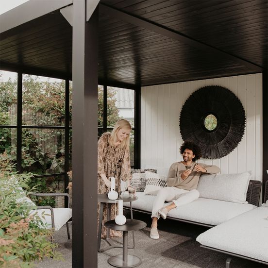 Een vrouw schenkt thee in een modern Hillhout buitenverblijf met loungebed in de tuin