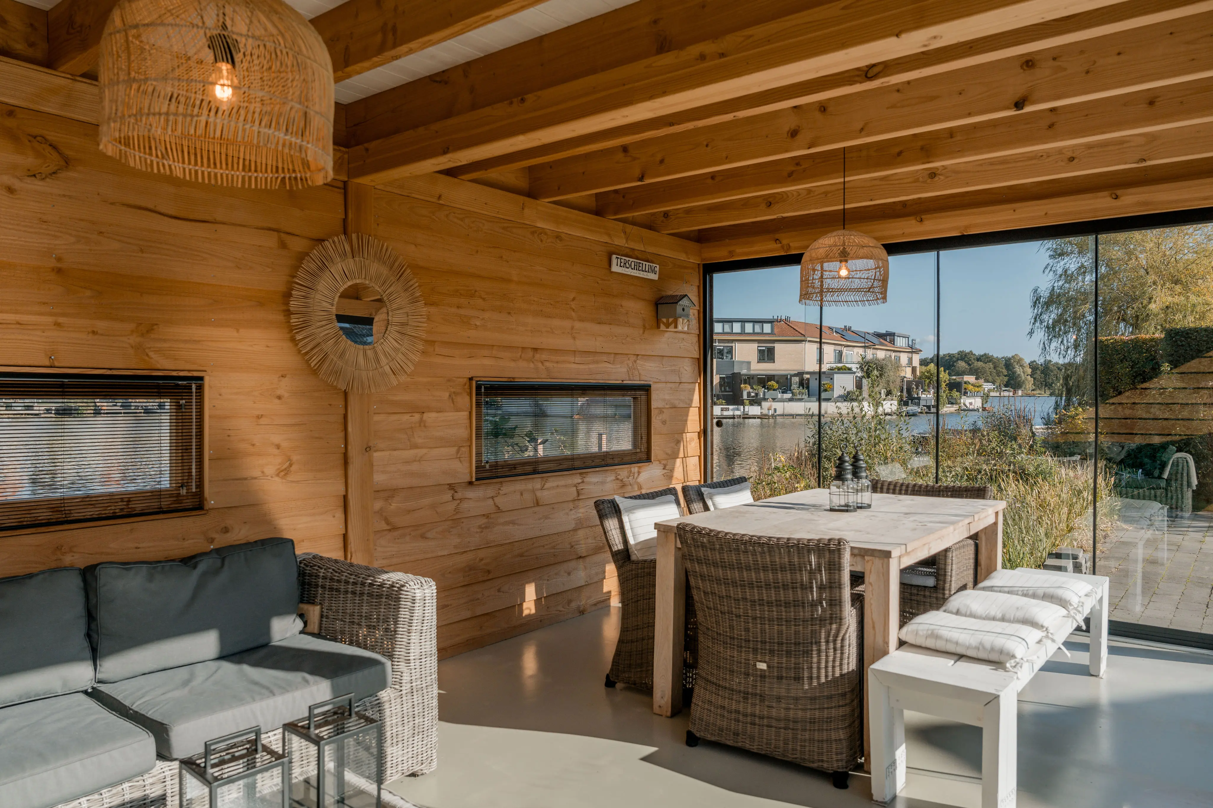 Interieur van een houten overkapping met eettafel en stoelen met uitzicht op het water