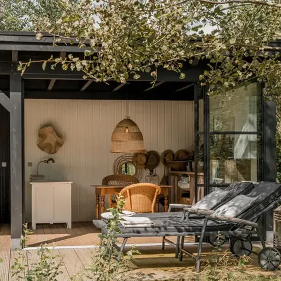 Houten buitenverblijf ingericht met loungestoelen en eettafel