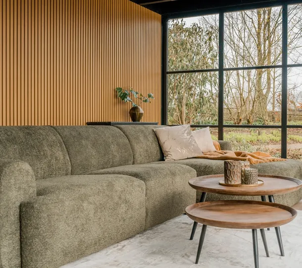 Groene loungebank in een houten buitenverblijf met twee ronde bijzettafels