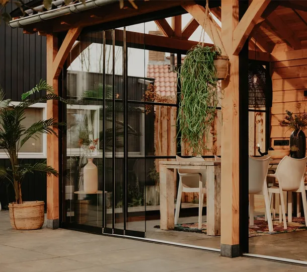 Close up van een houten buitenverblijf met zadeldak voorzien van glazenschuifwanden en tuinmeubilair
