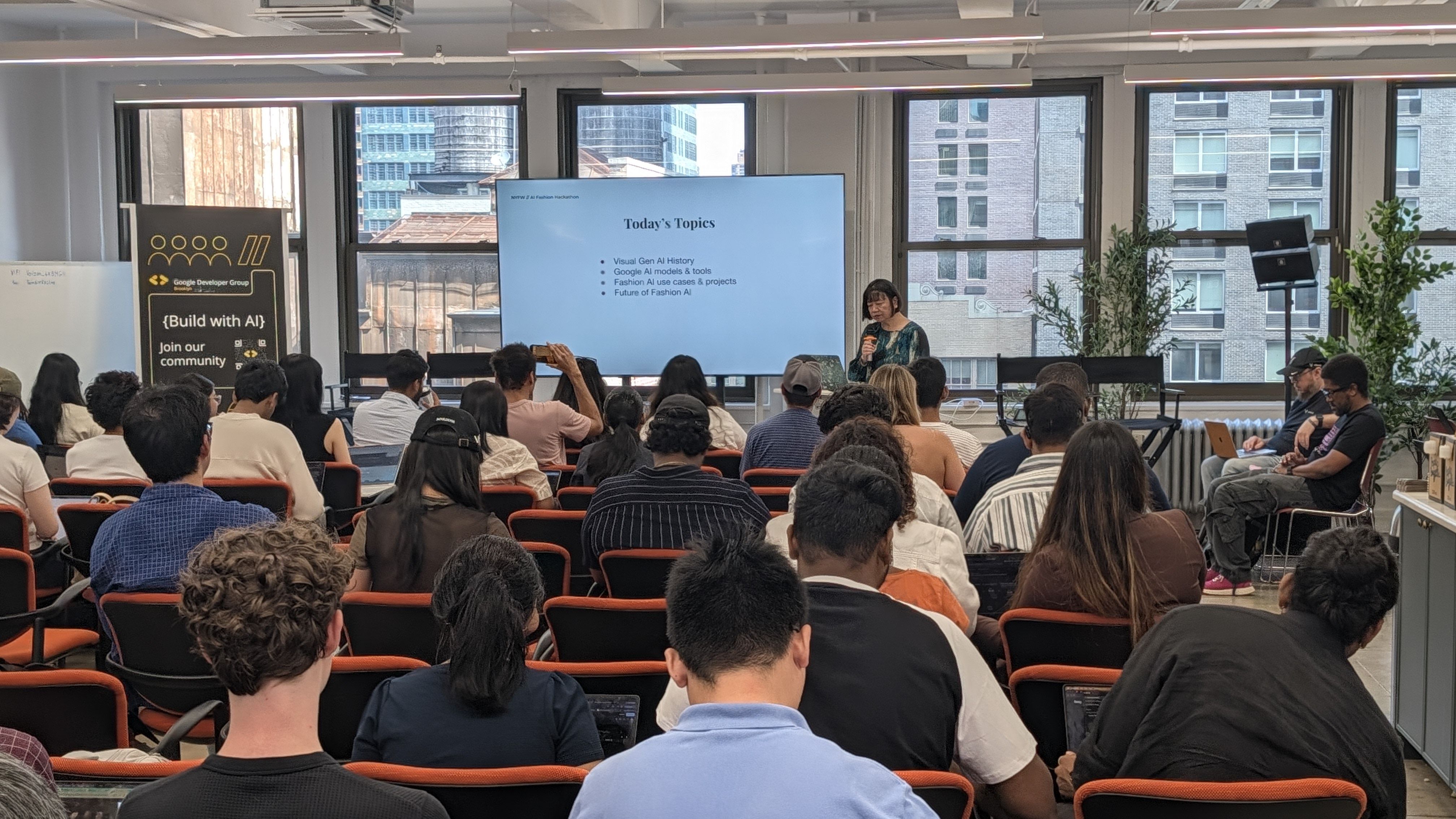 People attending a presentation on today's topics in AI, including history, tools, fashion use cases, and the future, in a modern conference room.