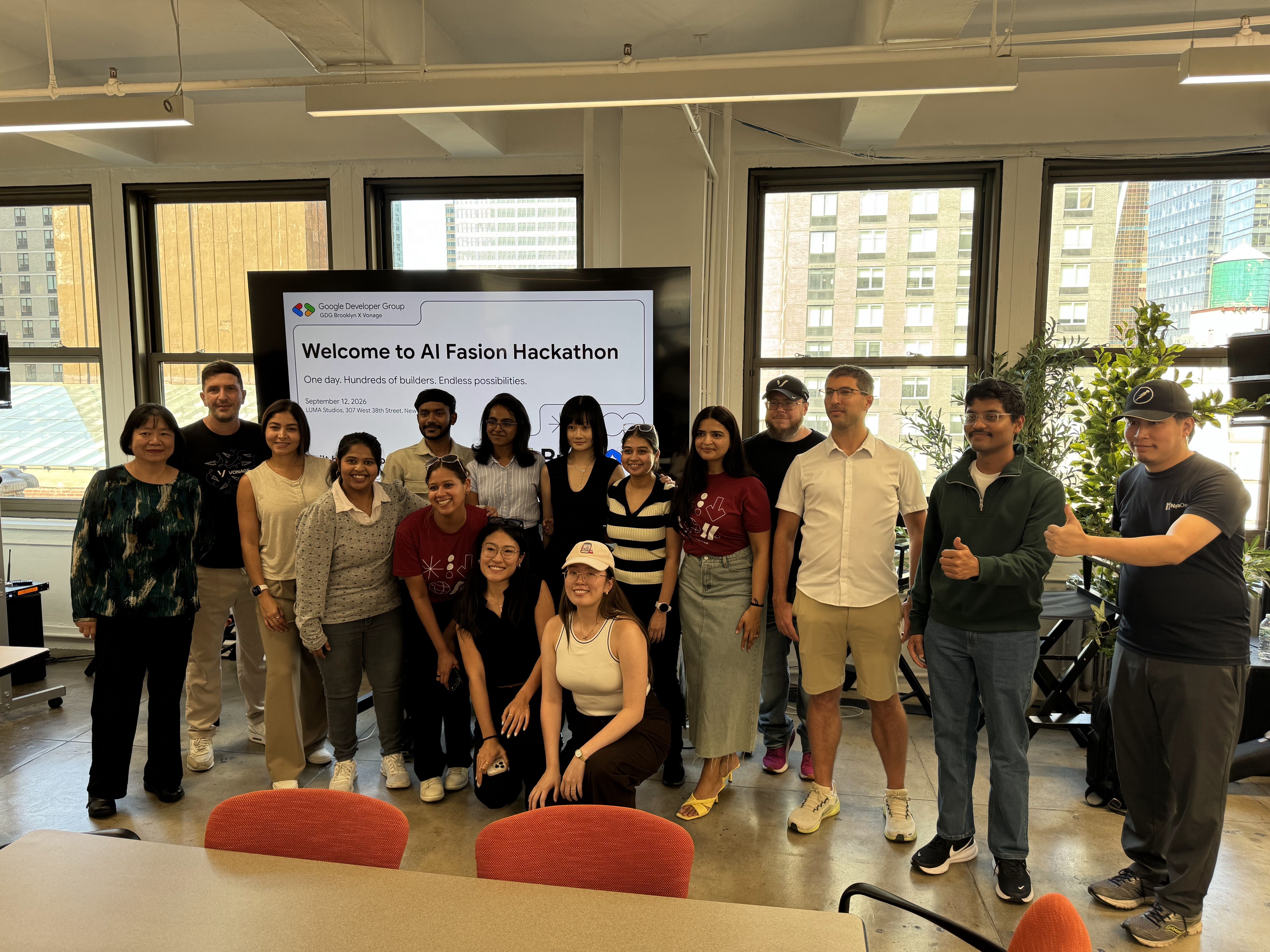 A group of people posing together in an office setting next to a screen displaying "AI Fashion Hackathon."